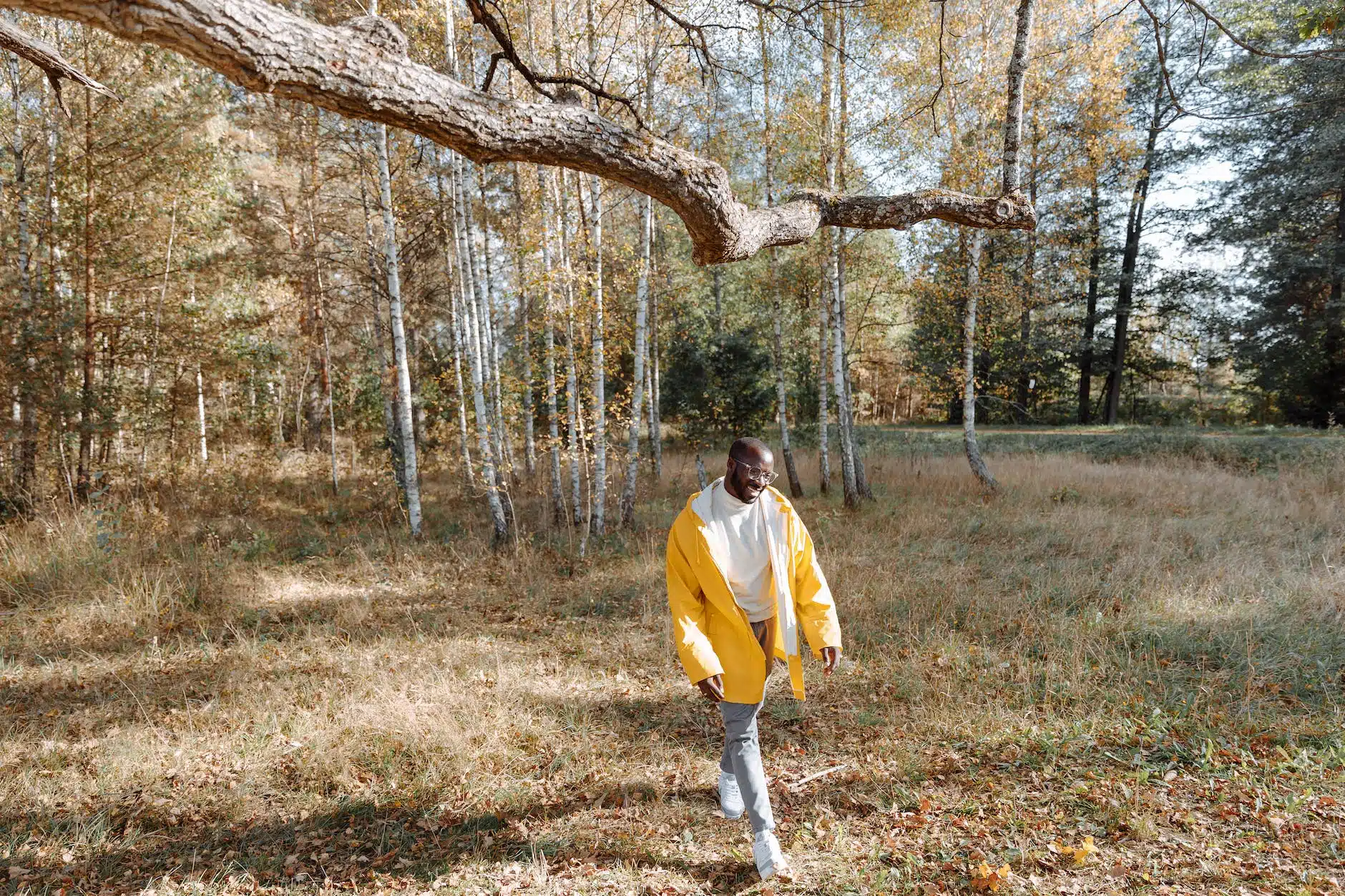 man in yellow long sleeve jacket and denim pants walking on a grass field