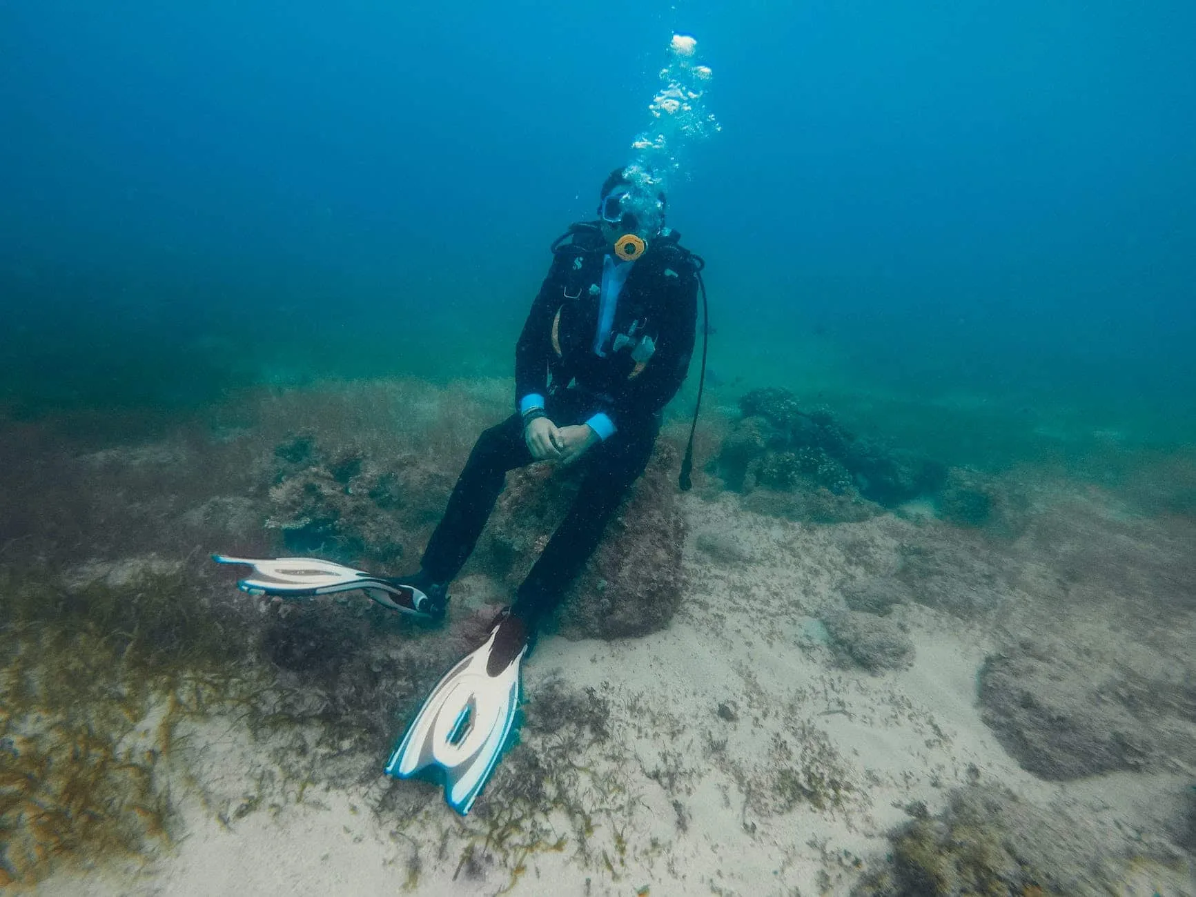 unrecognizable diver in diving suit sitting on stone under water