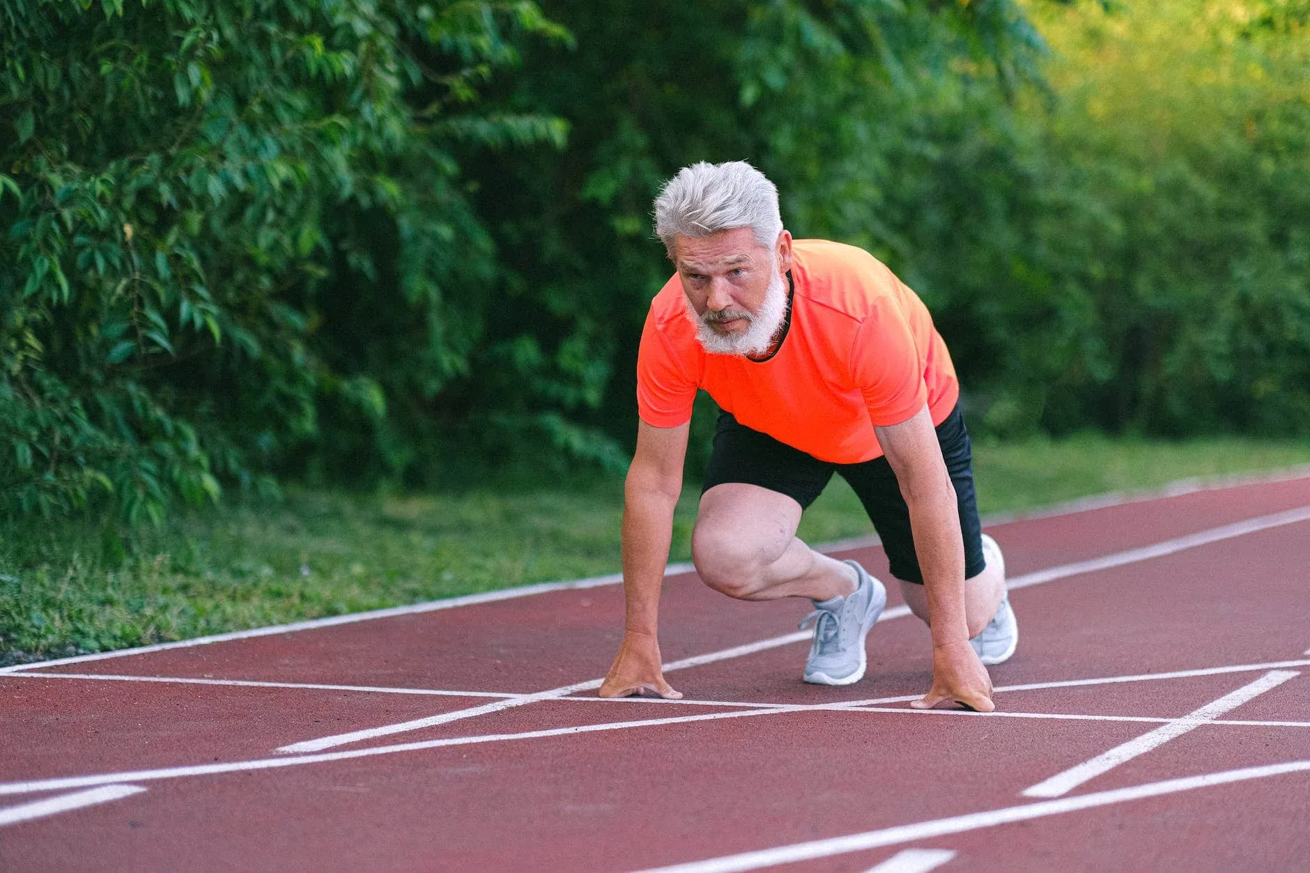 serious strong elderly man starting for run in racetrack